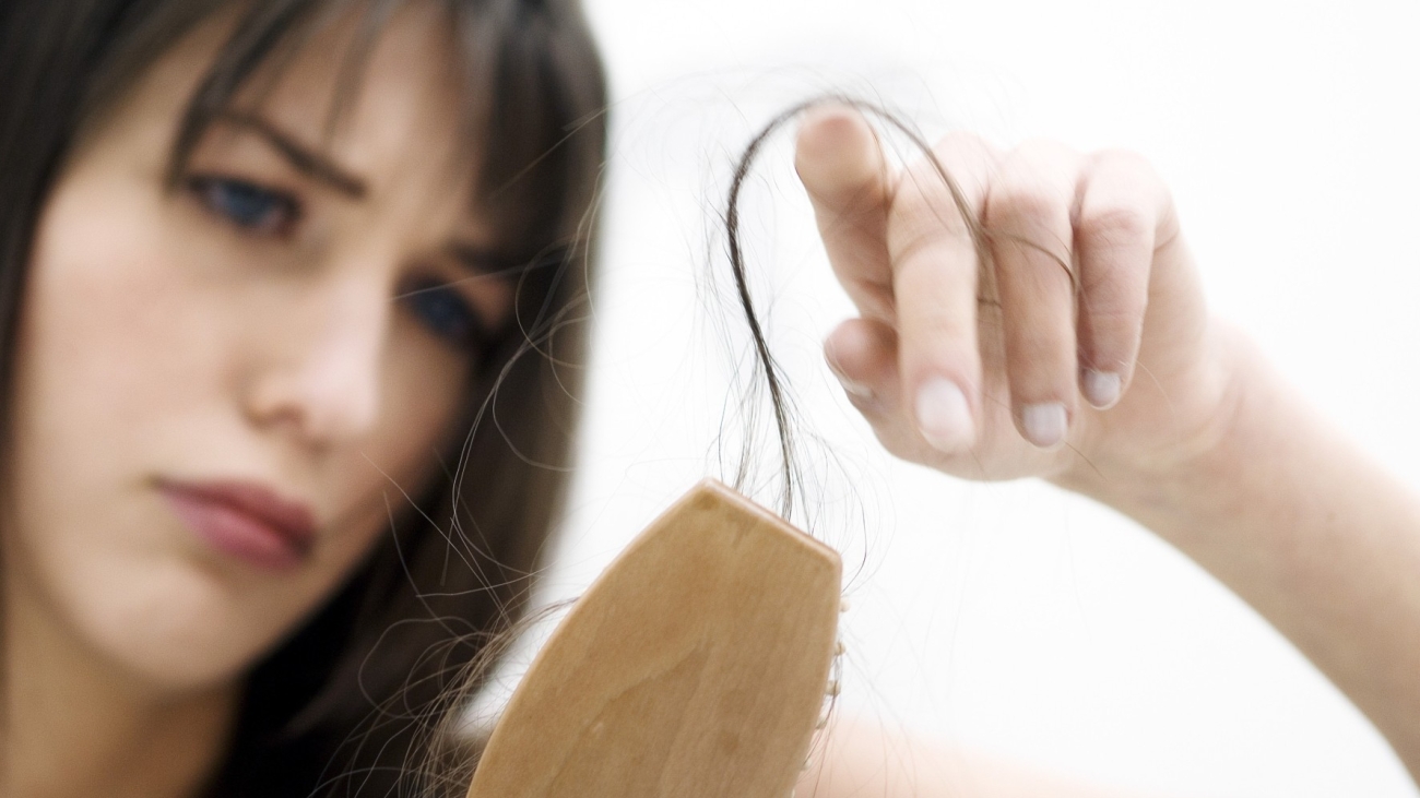 Portrait of a young woman brushing her hair, close up (studio)